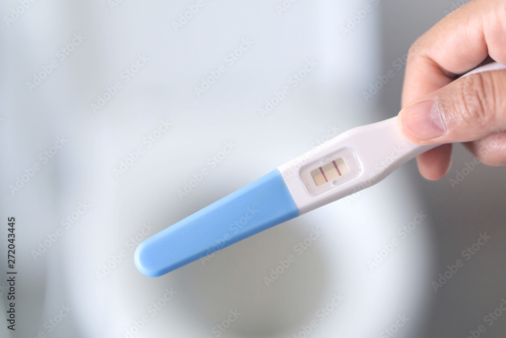 Obraz premium Closeup woman hand holding pregnancy test in bathroom, health care concept, selective focus