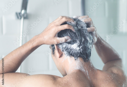 Closeup young man washing hair with with shampoo in the bathroom, vintage tone, selective focus photo