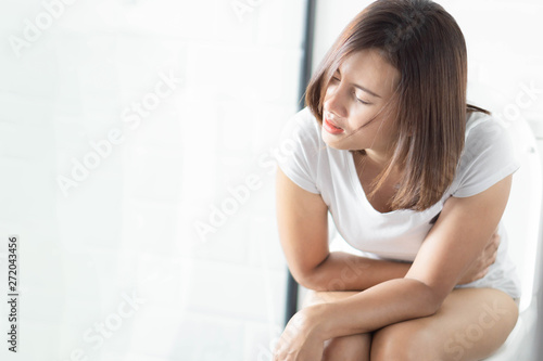 Closeup woman sitting on toilet in the morning with stomach ache, selective focus
