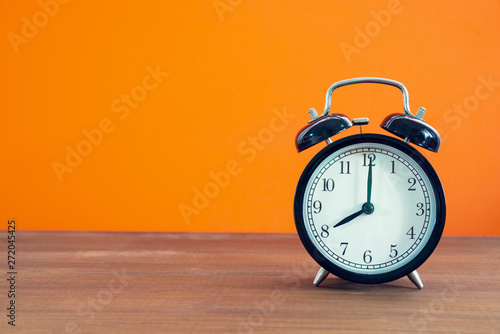 Retro alarm clock on wooden table with orange color background, vintage style