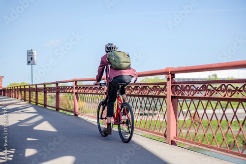 Woman cyclist with backpack fan of bike rides along transport and pedestrian bridge with handrails photo