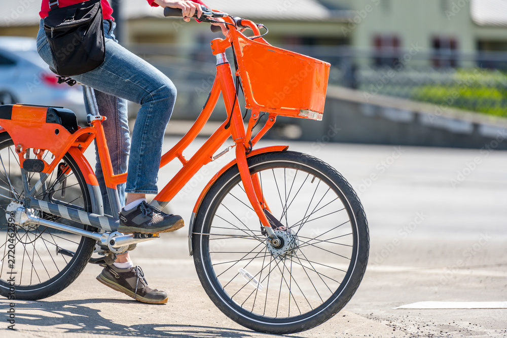 Naklejka premium Woman on an orange bike with basket waits at crossroads allowing traffic light