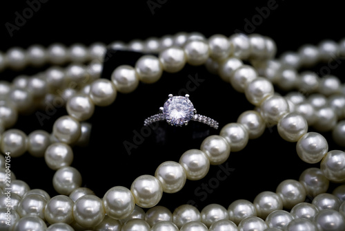 White crystal diamond ring and white brilliant pearl necklace beads on black background.