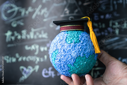 Education world, study learning achievement success in abroad global ideas. Graduation cap on models paper earth globe on hands, formula equation blackboard background. Congratulation in university
