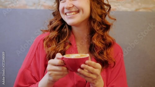 Pleasant leasure in coffee shop. Laughing happy woman drinking latte from a red mug.