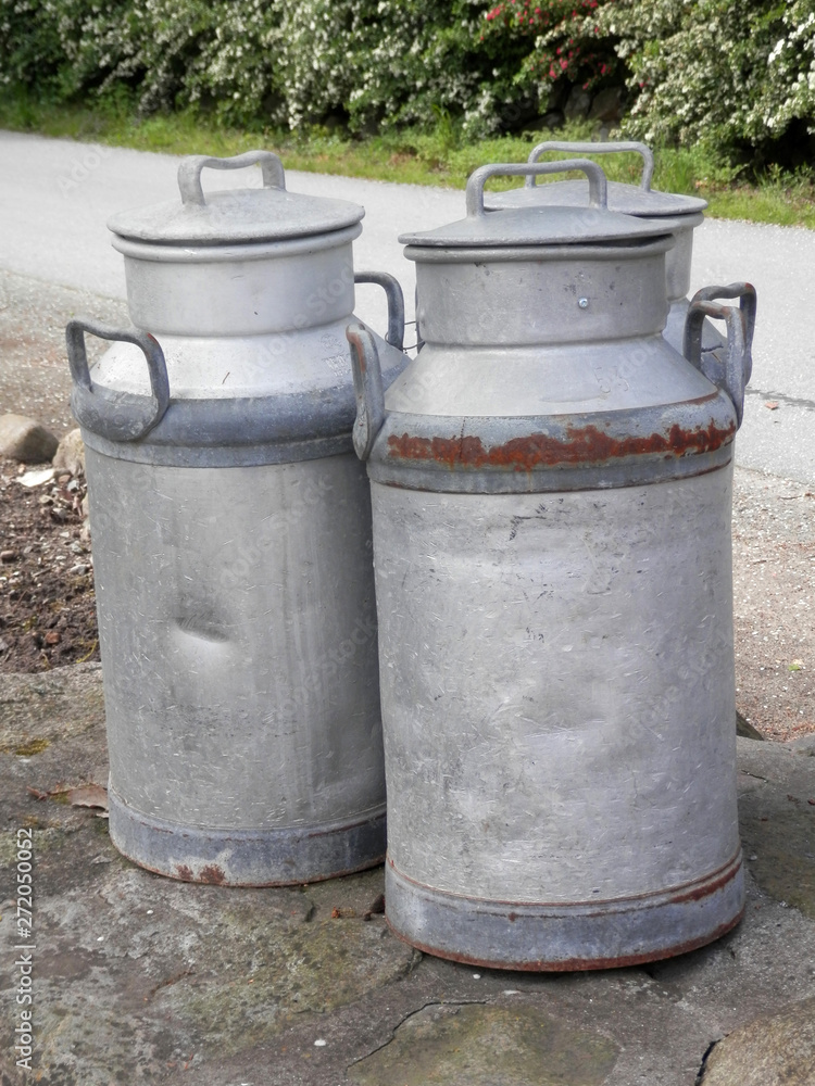 Rusty and battered old milk churns on village lane Rusty and battered old milk churns on village lane