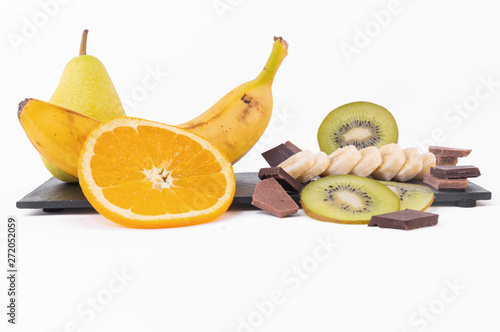 A mix of sliced kiwis and oranges, whole banana, chocolate and on a bright background