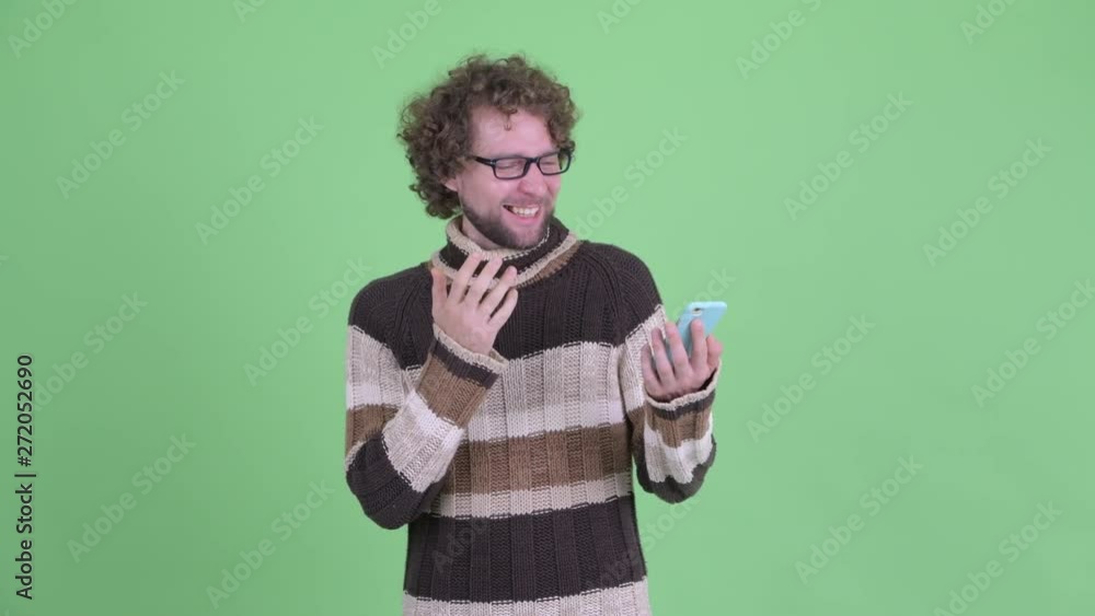 Happy young bearded man using phone and looking surprised Happy young bearded man using phone and looking surprised