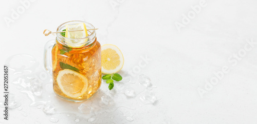 Iced tea with lemon slices and mint on light gray stone background.