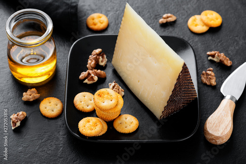 Manchego cheese with nuts, honey and crackers on black background.