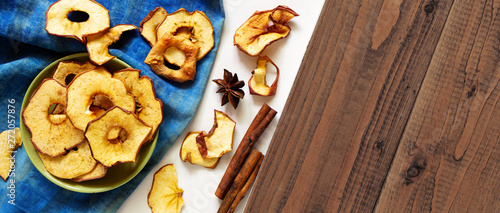 Dry apple chips and spices on white and brown wood background. Homemade baked sliced fruits, autumn fall healthy natural snack concept. Horizontal, top view, overhead, copy space.