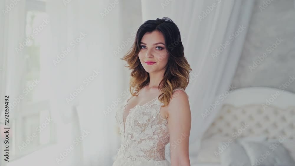 Sexy wedding lace dress on a beautiful model in the light studio. Attractive bride in luxurious dress with bouquet of flowers is coming to the window in bedroom. Sexy wedding lace dress on a beautiful model in the light studio. Attractive bride in luxurious dress with bouquet of flowers is coming to the window in bedroom.