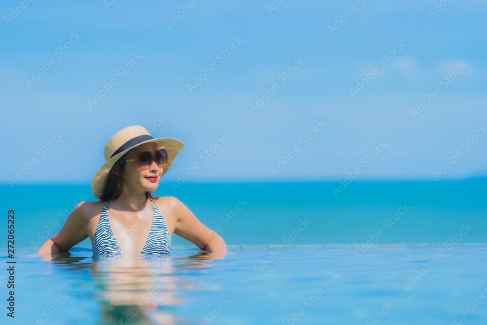 Portrait beautiful young asian woman happy smile relax in swimming pool at hotel resort neary sea ocean beach on blue sky
