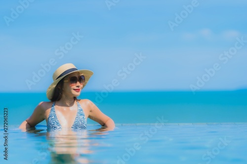 Portrait beautiful young asian woman happy smile relax in swimming pool at hotel resort neary sea ocean beach on blue sky © siraphol