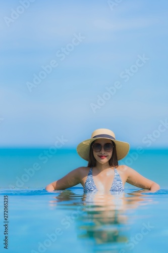 Portrait beautiful young asian woman happy smile relax in swimming pool at hotel resort neary sea ocean beach on blue sky © siraphol
