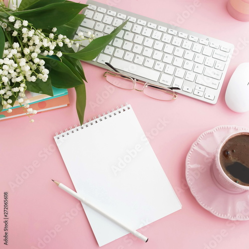 Pink flat lay top view women's office desk . Female workspace with laptop, white spring flowers lilies in a vase, accessories, notebooks mock up, glasses, cup of coffee on pale pink background. 