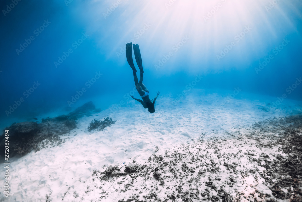 Young woman free diver glides over sandy sea with fins. Freediving in blue ocean - obrazy, fototapety, plakaty 