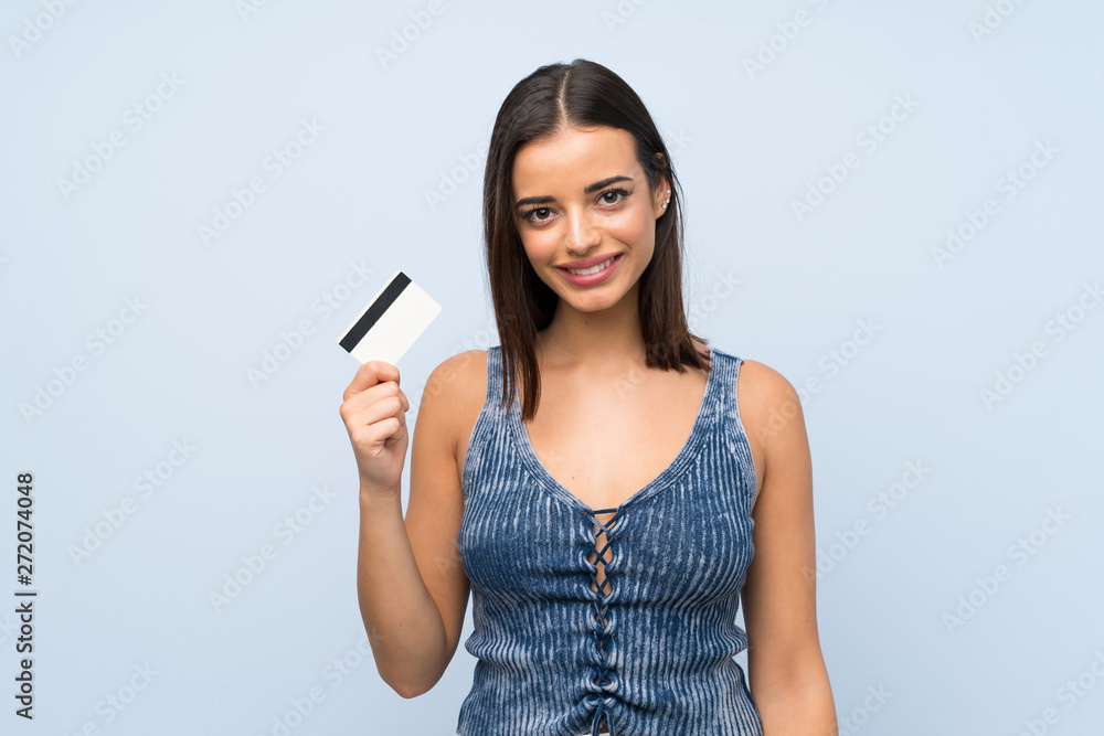 Young woman over isolated blue wall holding a credit card