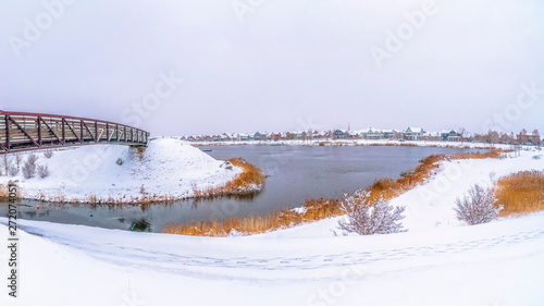 Panorama frame Panorama of a silvery lake with snow covered shore and metal bridge