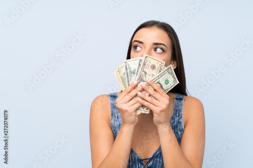 Young woman over isolated blue wall taking a lot of money
