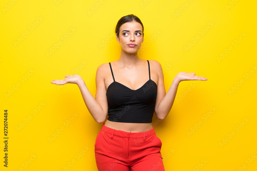 Young woman over isolated yellow background having doubts while raising hands Young woman over isolated yellow background having doubts while raising hands