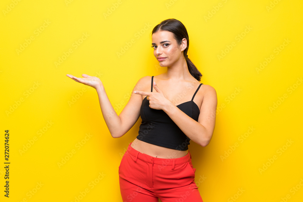 Young woman over isolated yellow background holding copyspace imaginary on the palm to insert an ad Young woman over isolated yellow background holding copyspace imaginary on the palm to insert an ad