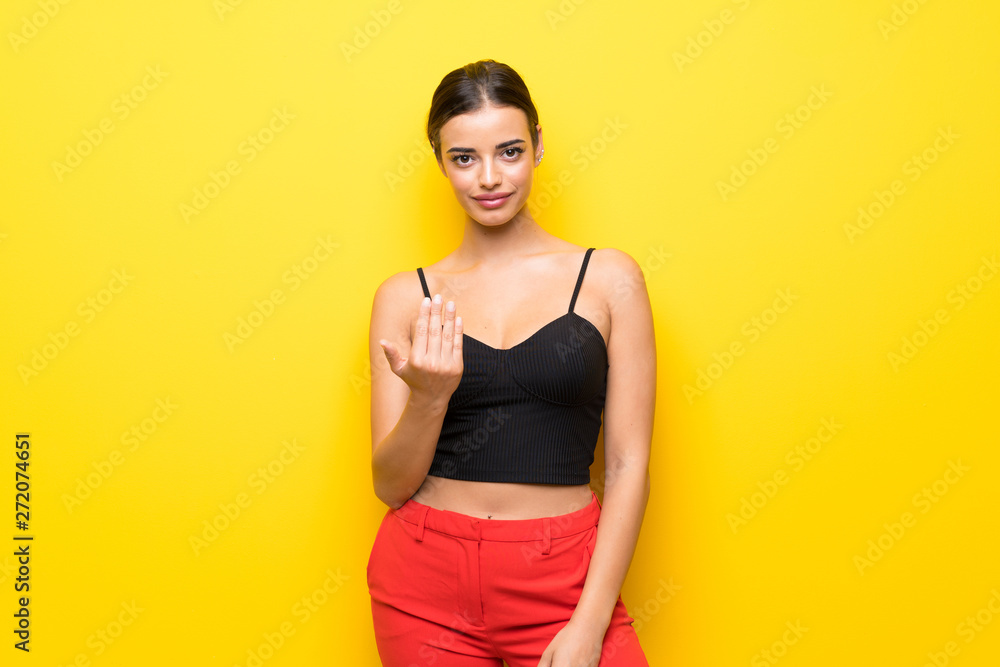 Young woman over isolated yellow background inviting to come with hand. Happy that you came Young woman over isolated yellow background inviting to come with hand. Happy that you came