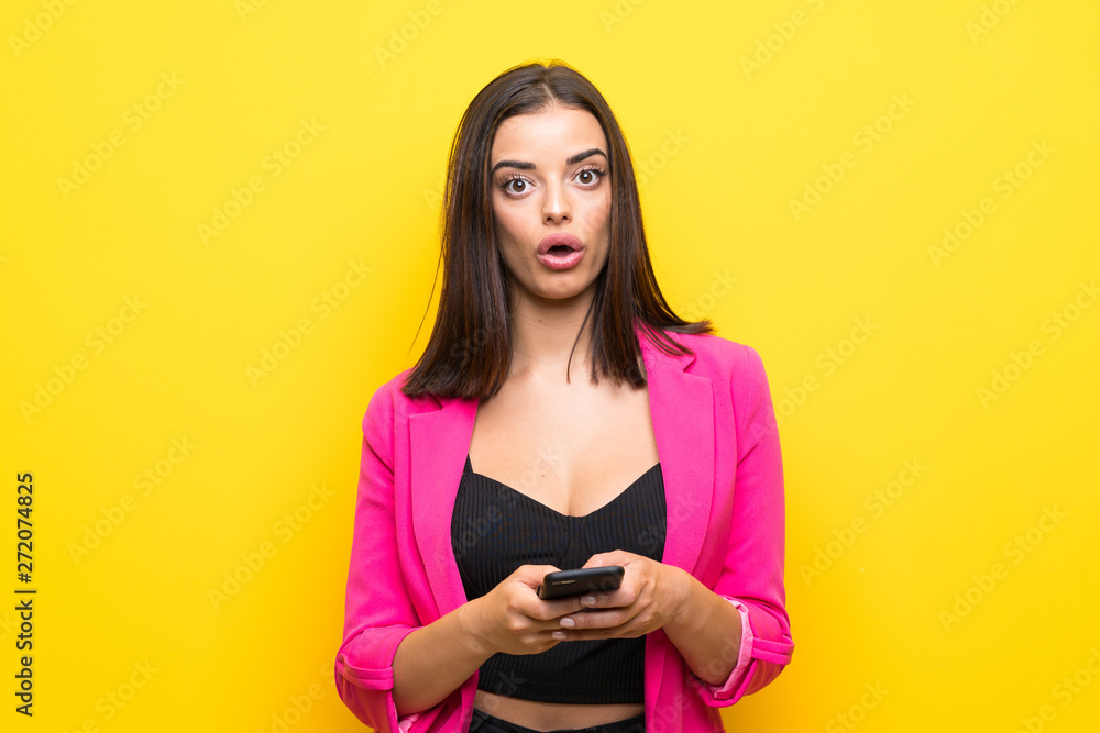 Young woman over isolated yellow background surprised and sending a message Young woman over isolated yellow background surprised and sending a message