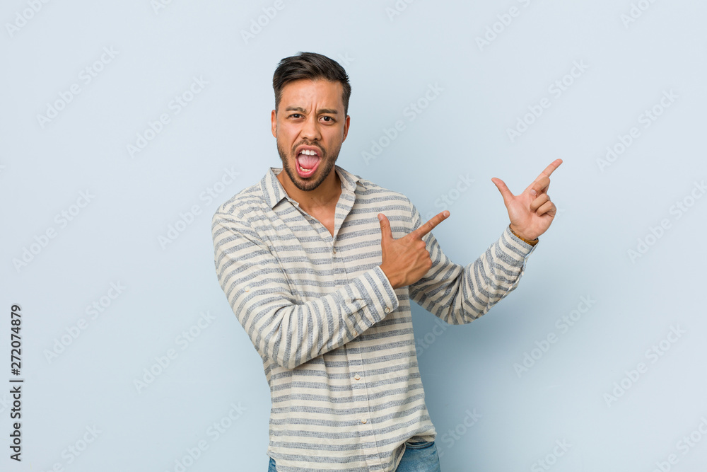 Young handsome filipino man pointing with forefingers to a copy space, expressing excitement and desire. Young handsome filipino man pointing with forefingers to a copy space, expressing excitement and desire.