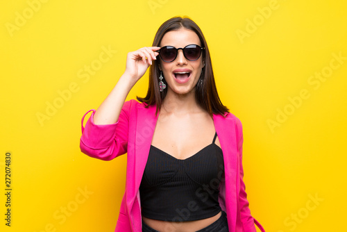 Young woman over isolated yellow background with glasses and surprised