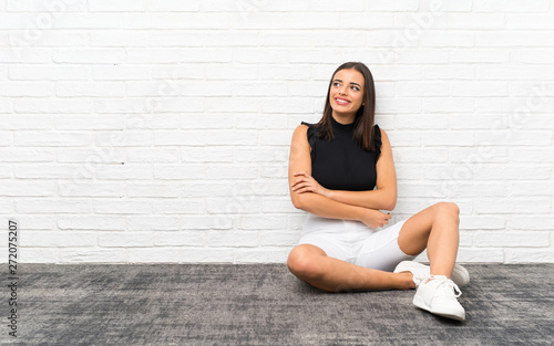 Pretty young woman sitting on the floor looking up while smiling