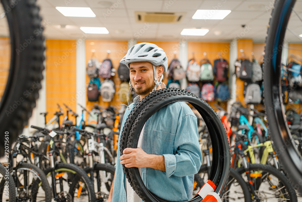Man in cycling helmet holds bicycle tyre, shopping