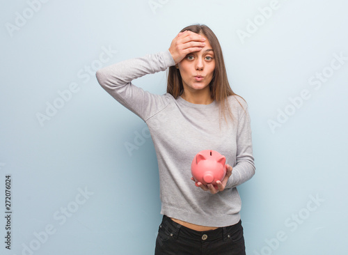 Young pretty caucasian woman worried and overwhelmed. She is holding a piggy bank.