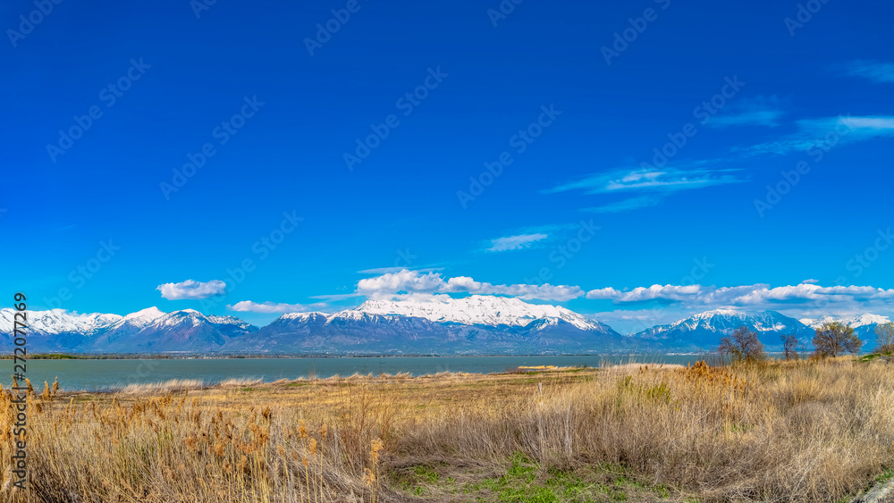 Panorama frame Panorama of a mountain with snowy peak towering over a lake with grassy shore Panorama frame Panorama of a mountain with snowy peak towering over a lake with grassy shore