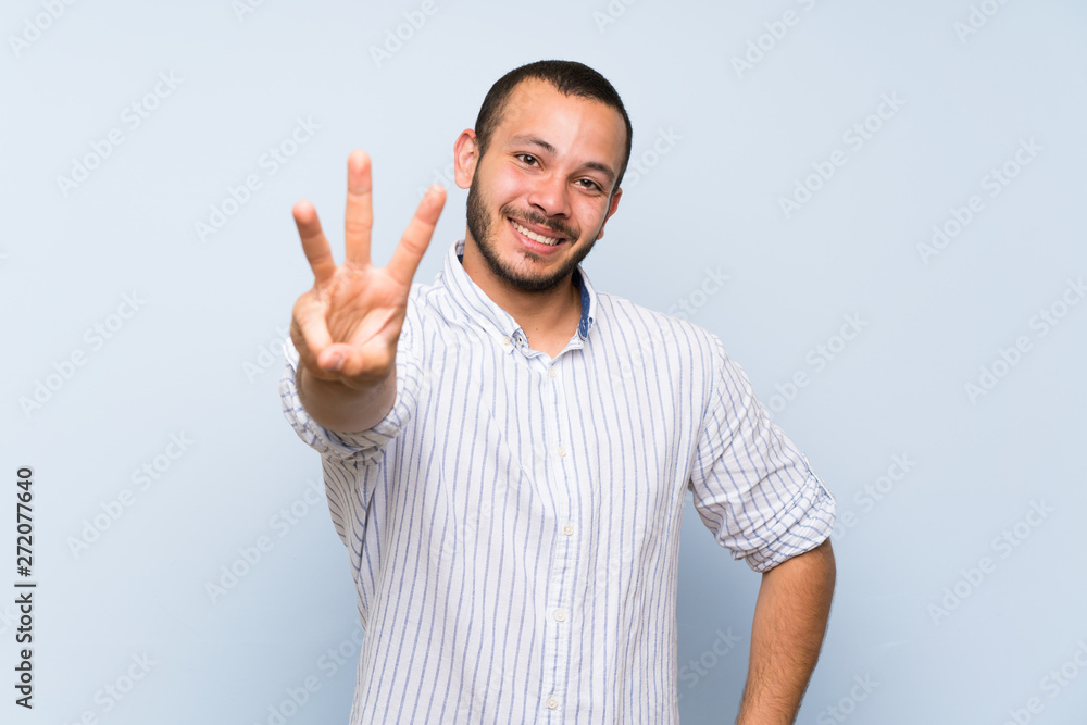 Colombian man over isolated blue wall happy and counting three with fingers Colombian man over isolated blue wall happy and counting three with fingers