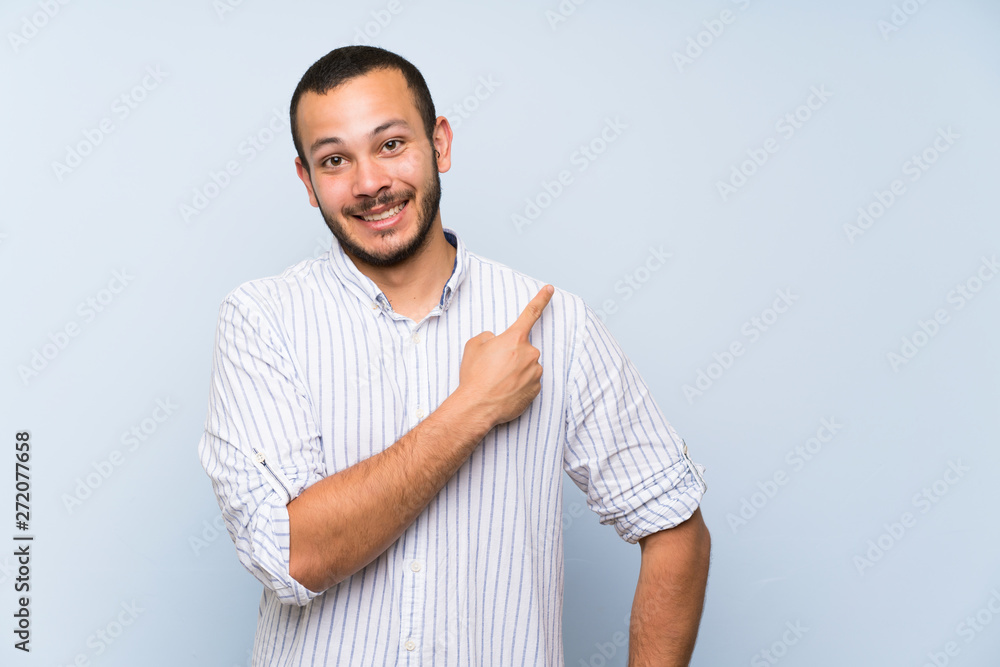 Fototapeta premium Colombian man over isolated blue wall pointing to the side to present a product