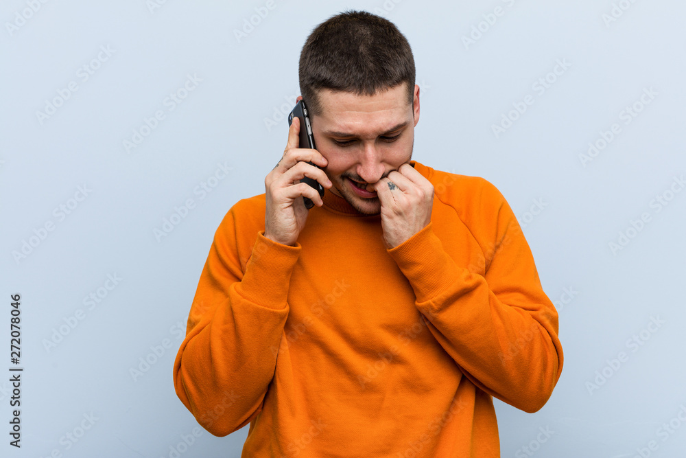 Young caucasian man holding a phone biting fingernails, nervous and very anxious. Young caucasian man holding a phone biting fingernails, nervous and very anxious.