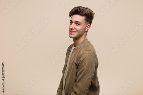 Young caucasian man wearing a brown jacket looks aside smiling, cheerful and pleasant.