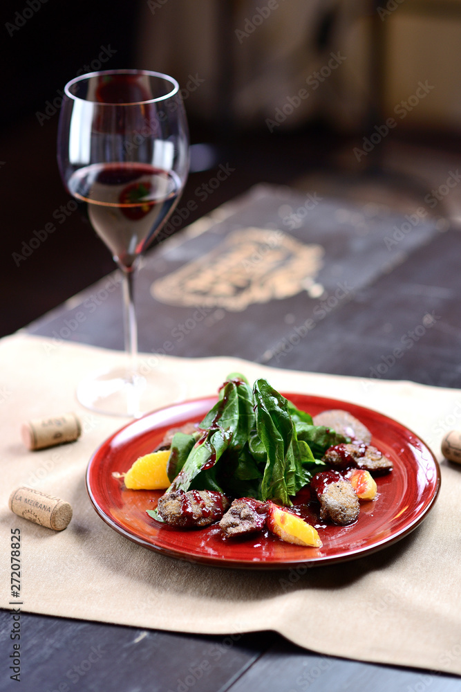 salad with liver, spinach and orange on a red plate, on a wooden table