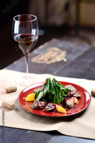 salad with liver, spinach and orange on a red plate, on a wooden table