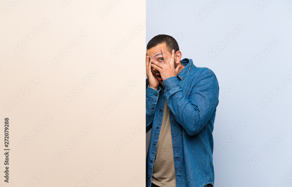Colombian man holding an empty placard covering eyes and looking through fingers Colombian man holding an empty placard covering eyes and looking through fingers