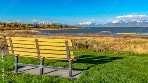 Panorama frame Bench on a grassy field facing a lake and snowy mountain against blue sky