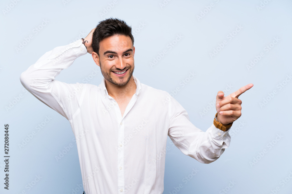 Handsome young man over isolated blue background surprised and pointing finger to the side Handsome young man over isolated blue background surprised and pointing finger to the side