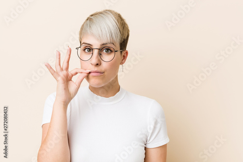 Fototapeta Naklejka Na Ścianę i Meble -  Young authentic natural woman wearing a white shirt with fingers on lips keeping a secret.