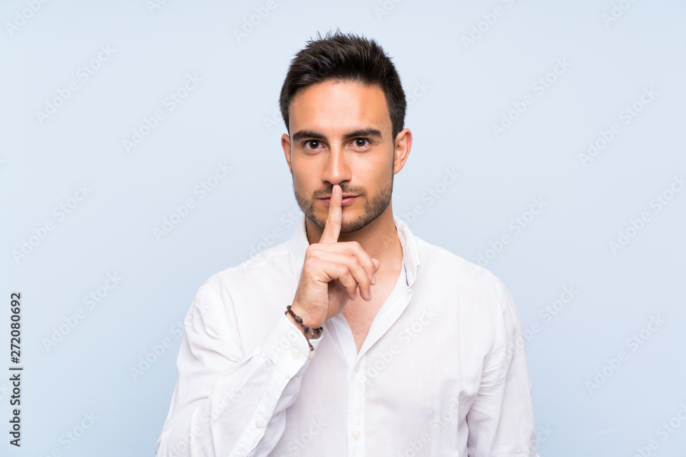Handsome young man over isolated blue background showing a sign of silence gesture putting finger in mouth Handsome young man over isolated blue background showing a sign of silence gesture putting finger in mouth