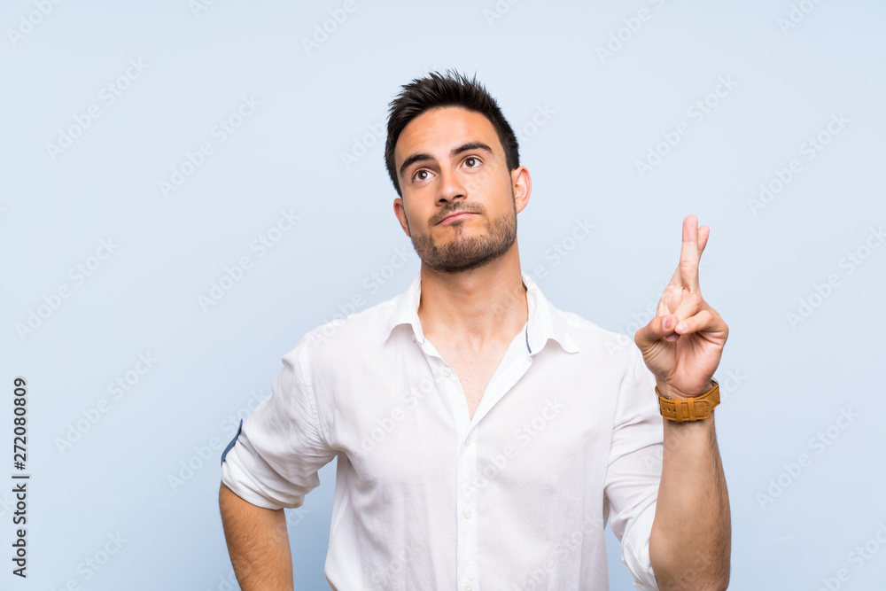Handsome young man over isolated blue background with fingers crossing and wishing the best Handsome young man over isolated blue background with fingers crossing and wishing the best