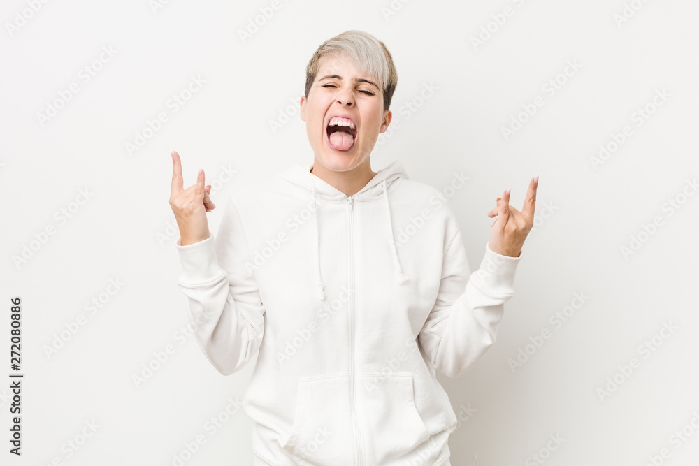 Young curvy woman wearing a white hoodie showing rock gesture with fingers Young curvy woman wearing a white hoodie showing rock gesture with fingers