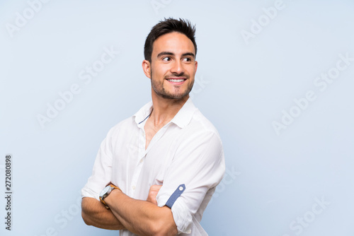 Handsome young man over isolated blue background with arms crossed and happy