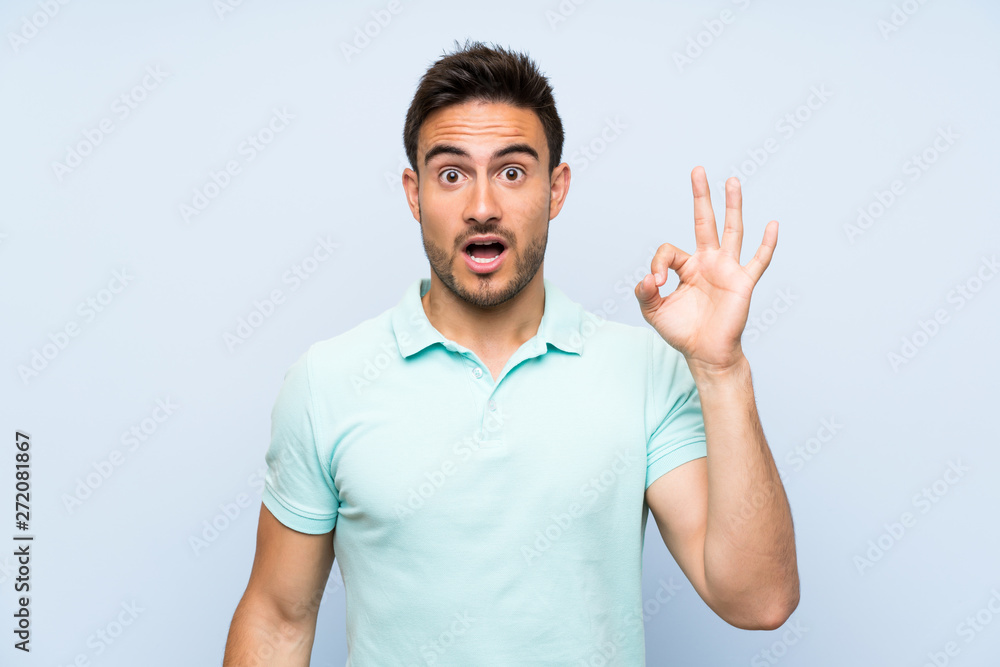 Handsome young man over isolated background surprised and showing ok sign Handsome young man over isolated background surprised and showing ok sign