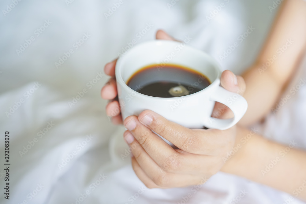 girl's hand hold cup of hot coffee on white bed girl's hand hold cup of hot coffee on white bed